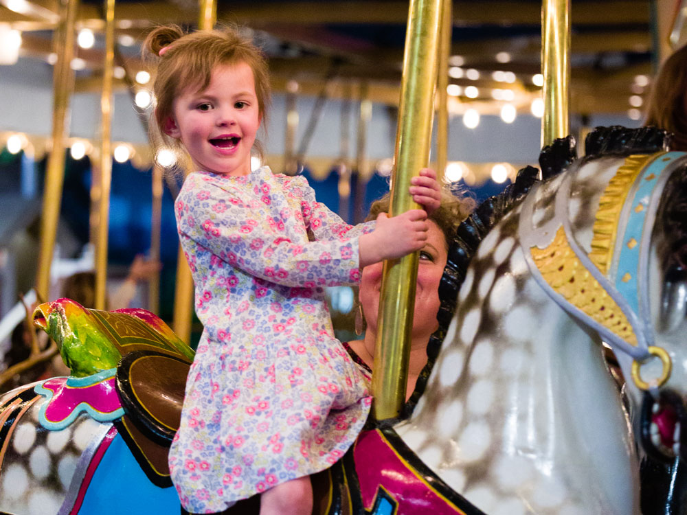 Young child smiling while riding Carousel horse.